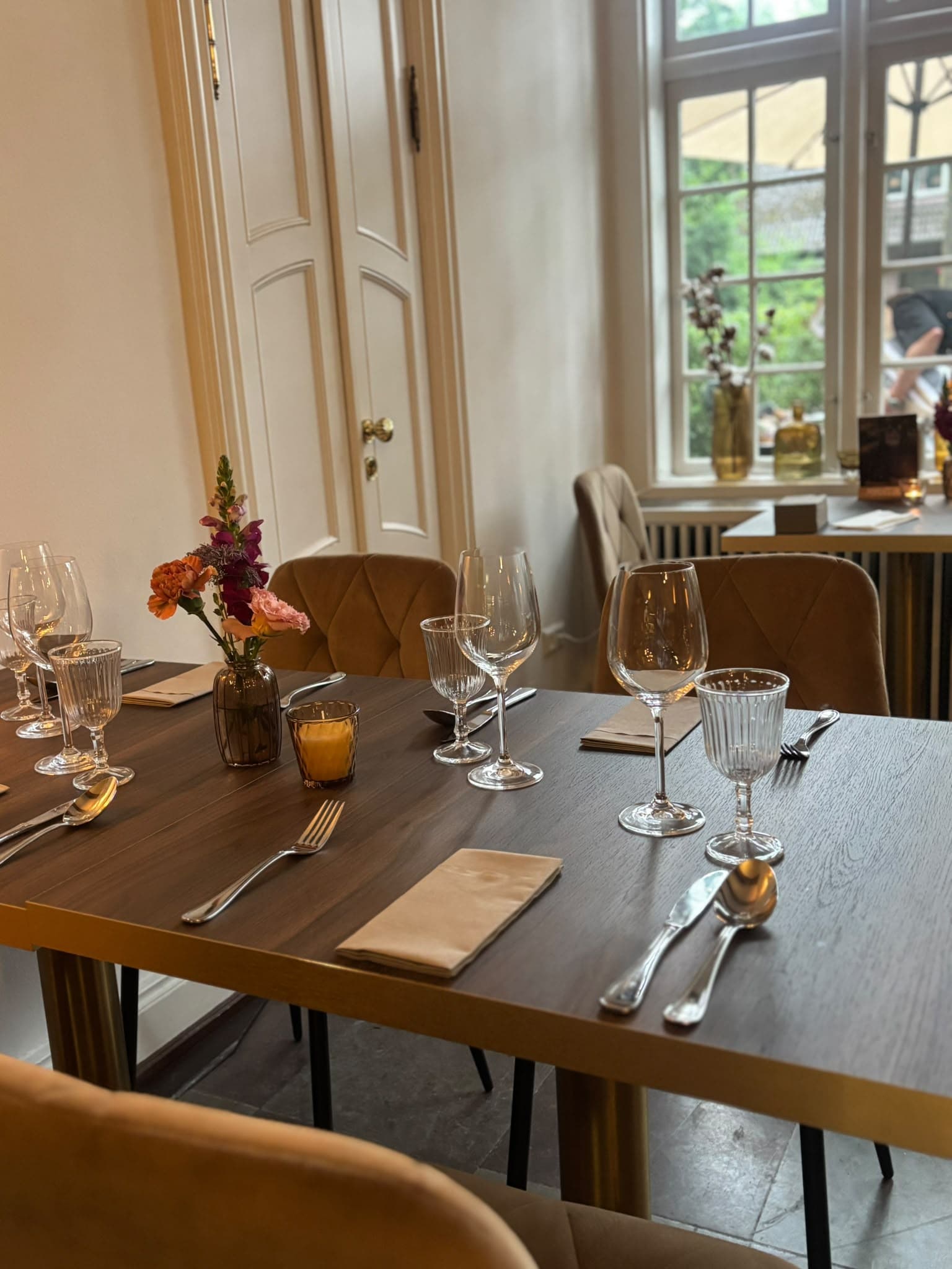 Eingedeckter Tisch mit Weingläsern, Blumen und Kerze, dahinter eine weiße Kassettentür und ein Fenster